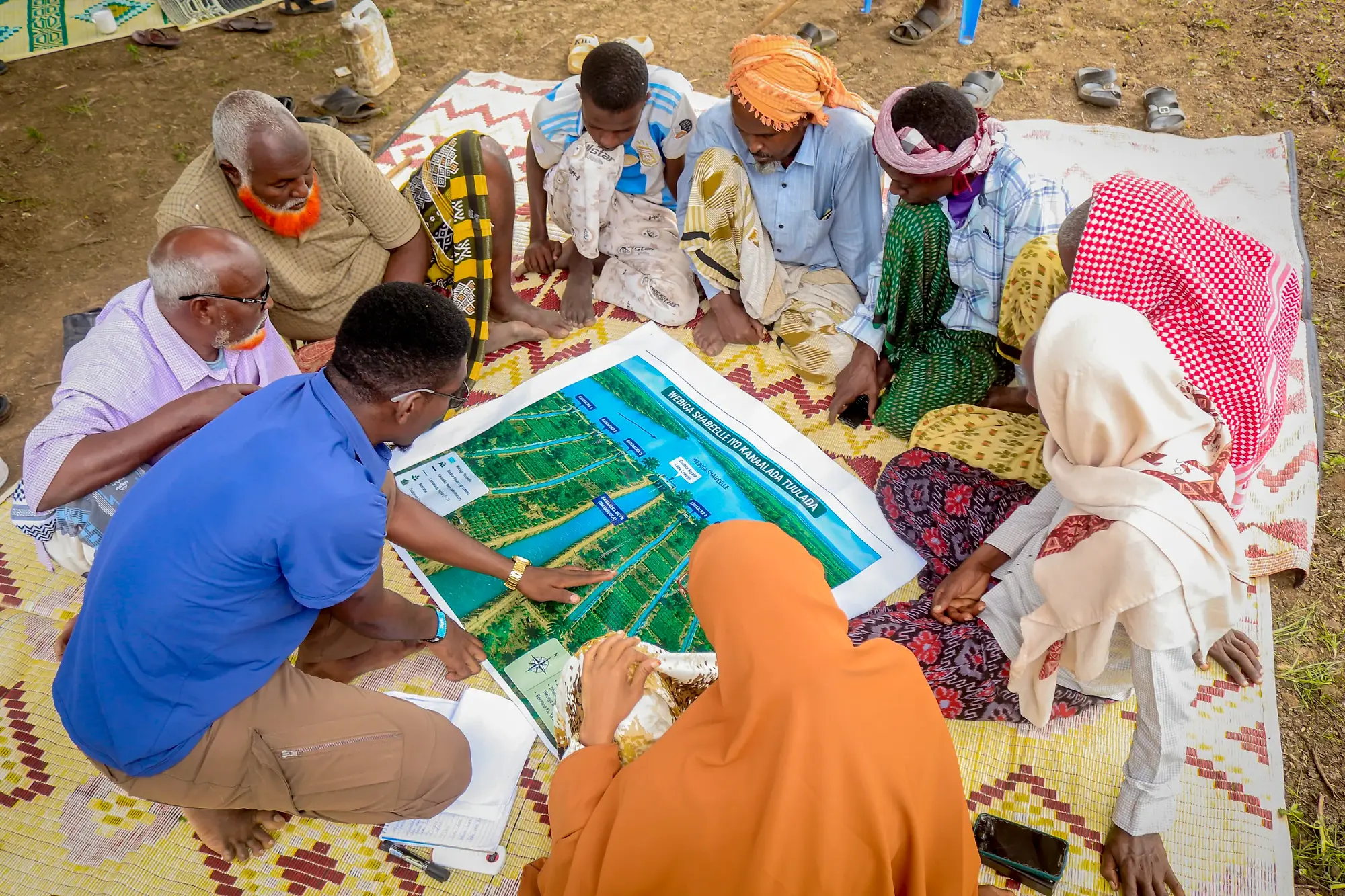 Hands and pens reaching across a large printed map spread out on a mat, several people annotating at once.
