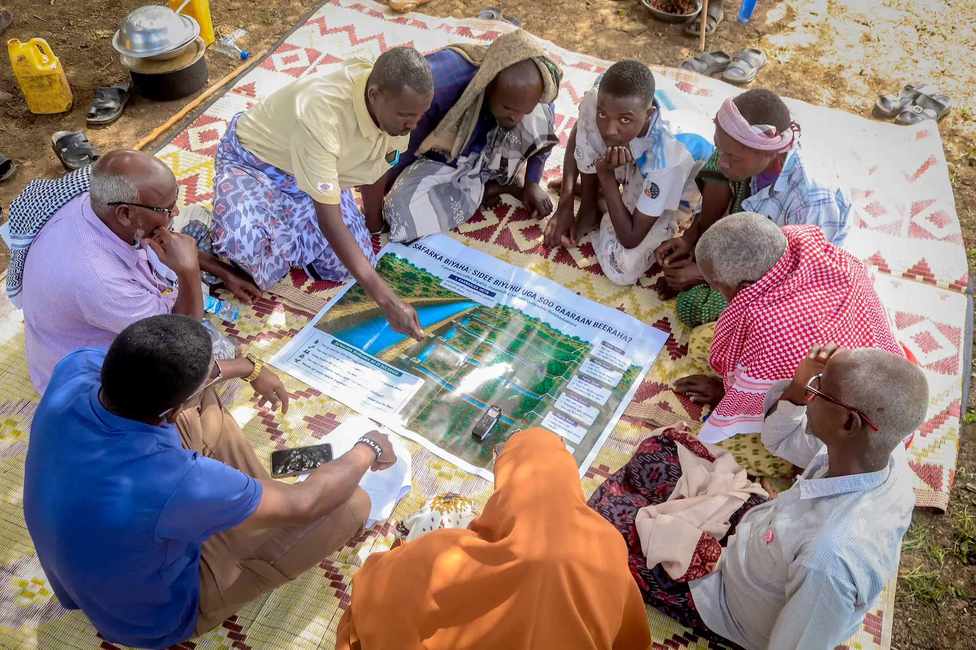 Participants kneeling over a printed community map on the mat, one writing on it.