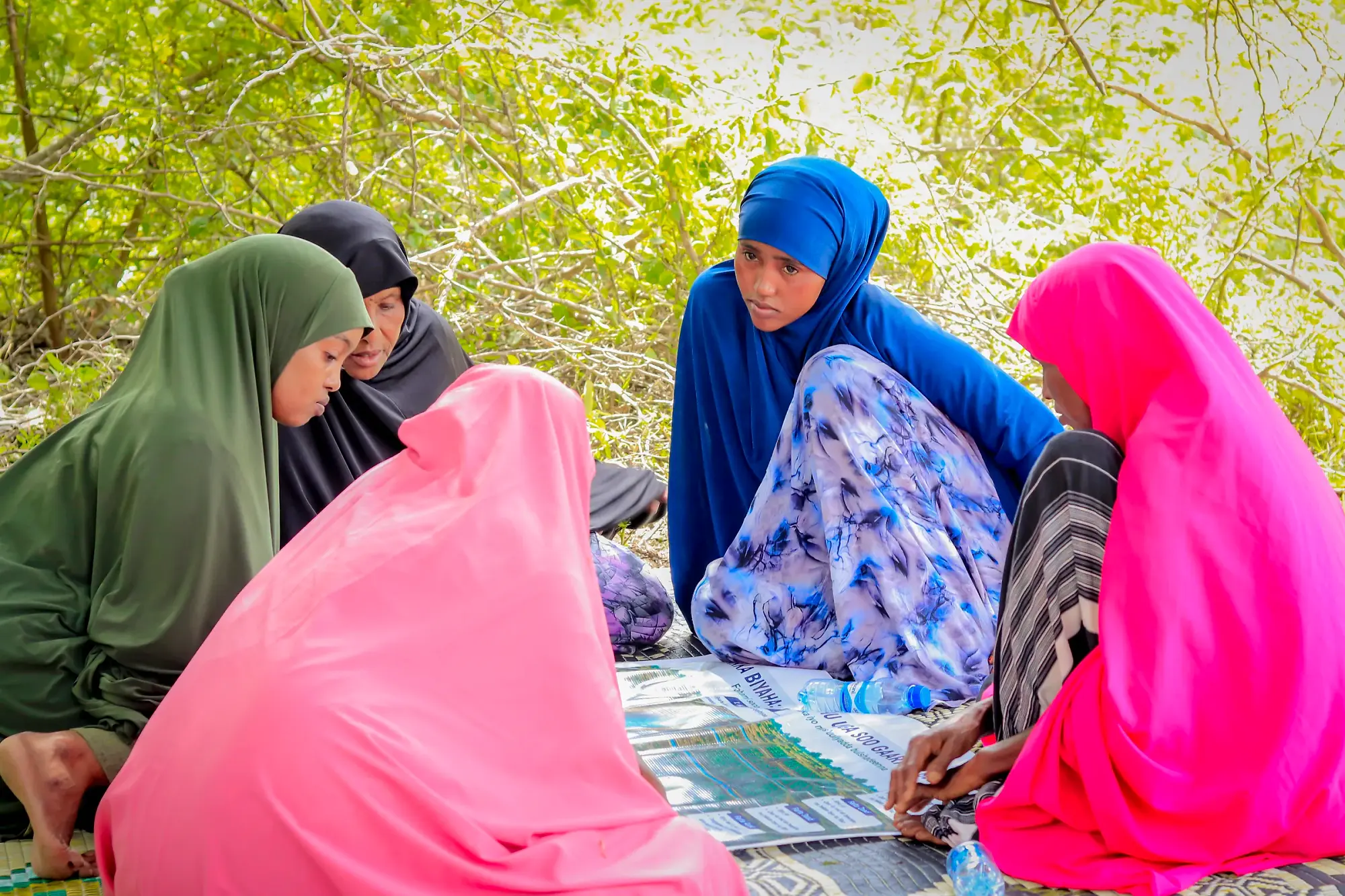 A women-only group seated on mats working over a large printed map, one writing.
