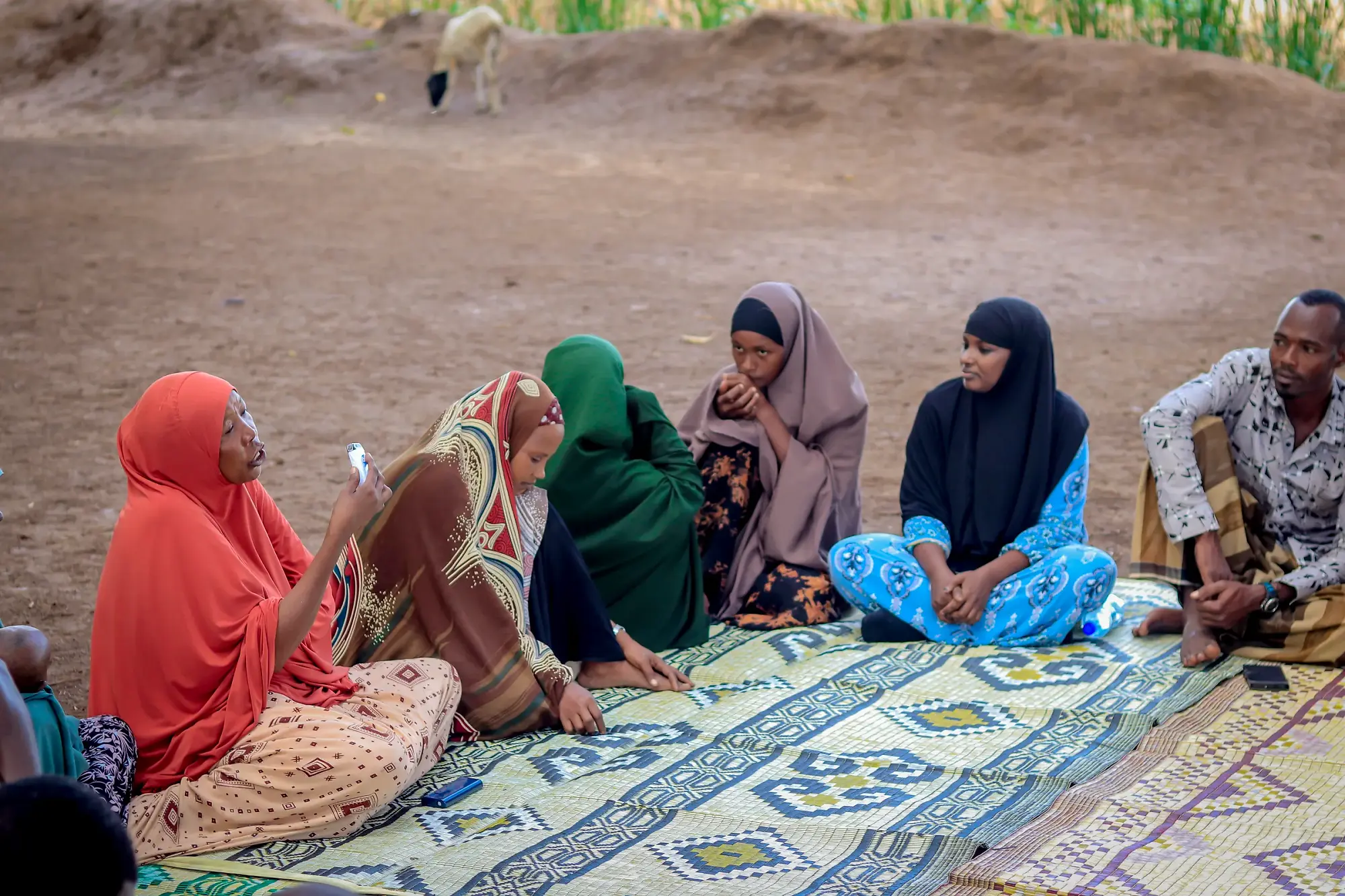 Four women seated close together on patterned mats, mid-conversation, one listening intently.